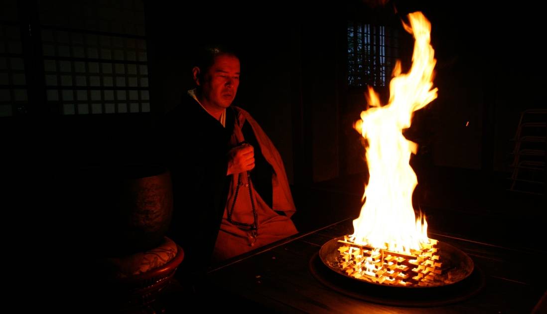 数珠を持ち、祈りを捧げている僧侶。護摩木を燃やす炎が高く燃え上がっている。